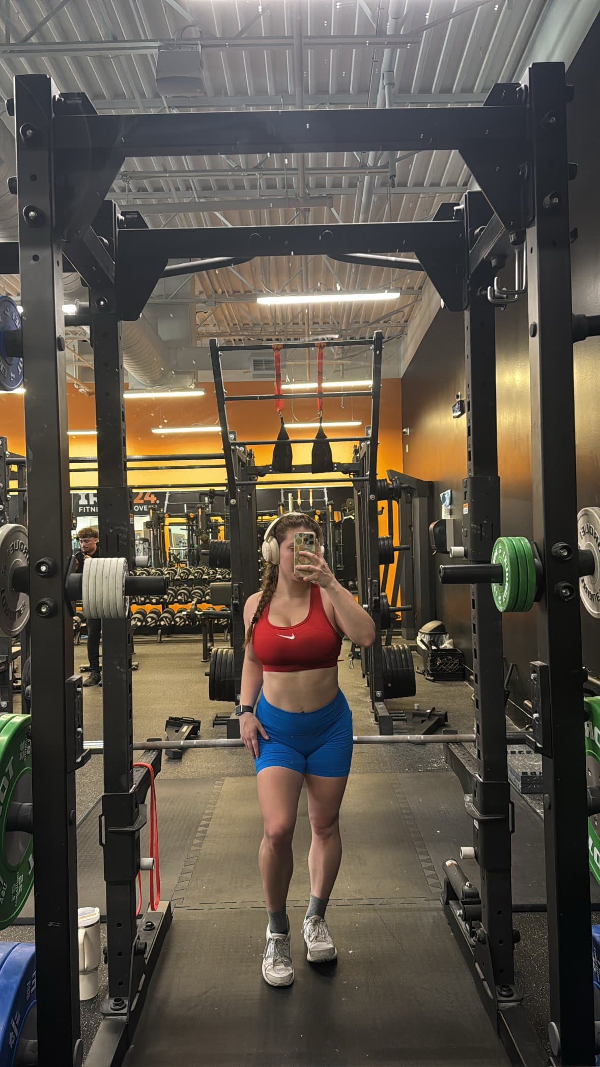 Jea mid-workout in the squat rack, headphones on, checking her programmed session